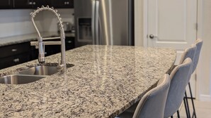 Eine Küche mit Granit-Arbeitsplatten, Edelstahlgeräten und Pendelleuchten.