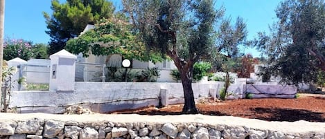 Eine Steinsäule, ein Baum und ein weißes Gebäude mit einem Zaun im Hintergrund.