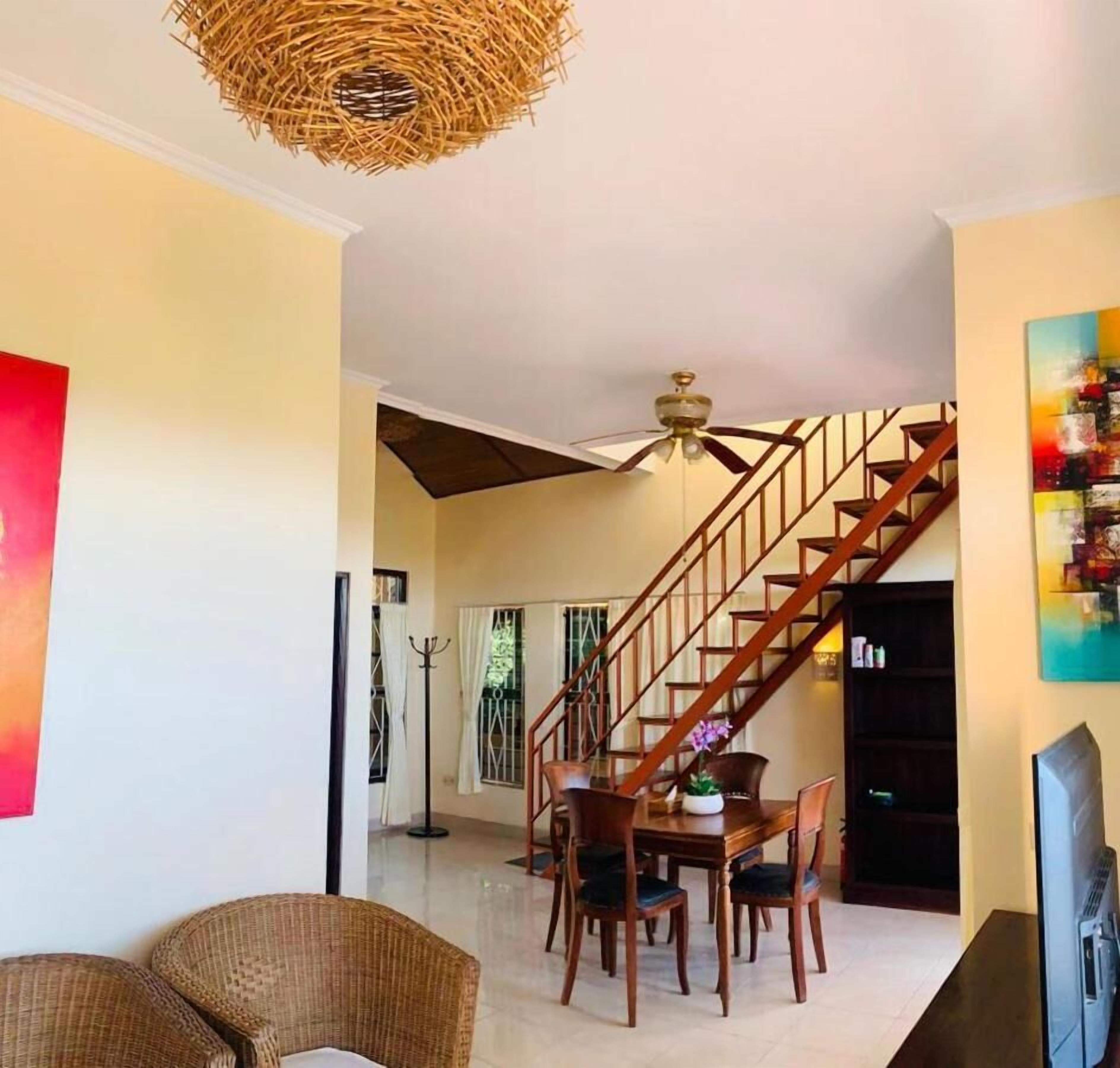 Un vaste espace de vie comprenant une table à manger, des chaises, un canapé, un escalier et un ventilateur de plafond.