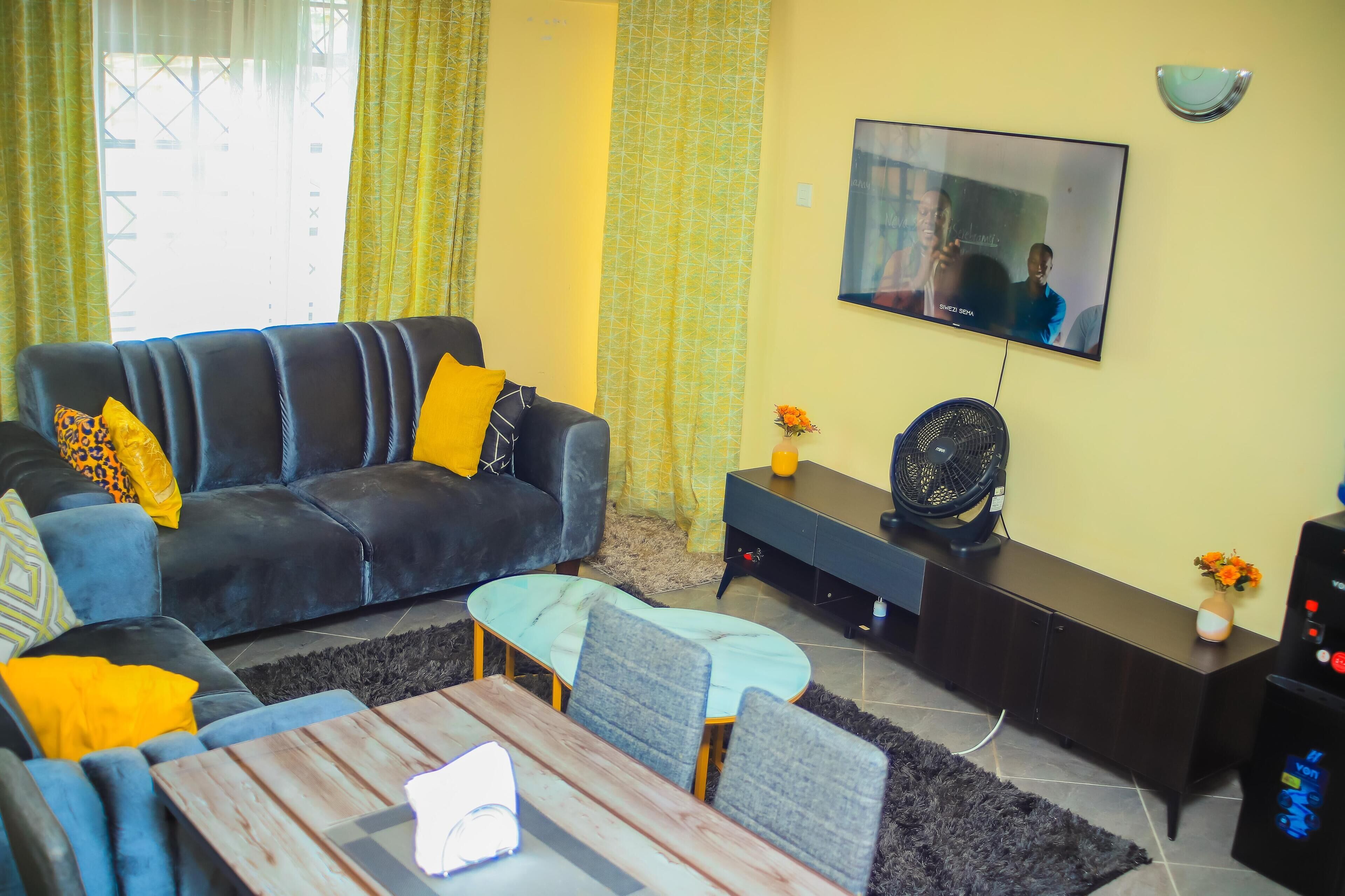 A living room with a sofa, coffee table, TV, and a fan.