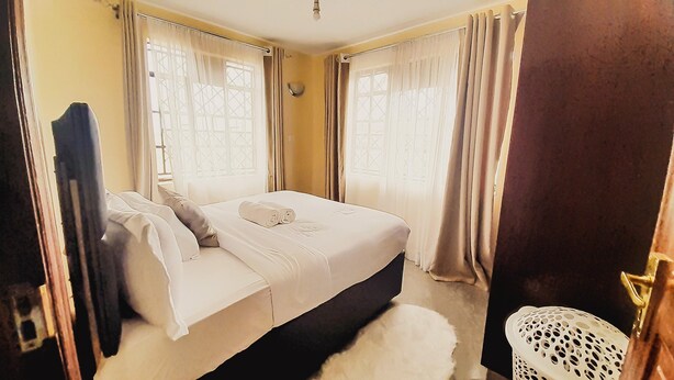 Une chambre à coucher avec un lit, des rideaux, une fenêtre et un petit panier blanc.