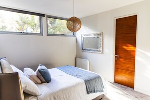 A bedroom with a bed, pillows, a hanging light fixture, a radiator, a door, and windows. - Panoramic Bay Views Mt Martha (Mount Martha)
