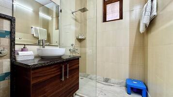 Un baño moderno con un espejo grande, un lavamanos blanco, una ducha y un taburete azul.
