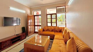 Ein Wohnzimmer mit einer Couch, einem Glastisch, einem an der Wand befestigten Fernseher und einem Deckenventilator.