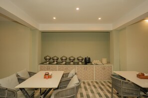 Un espace repas moderne avec une longue table et des chaises en osier, un buffet avec des distributeurs de nourriture et de boissons, et un sol orné d’un motif en chevrons.