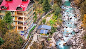 Un hotel de varios pisos con balcones, un río y una estructura pequeña con paneles solares.