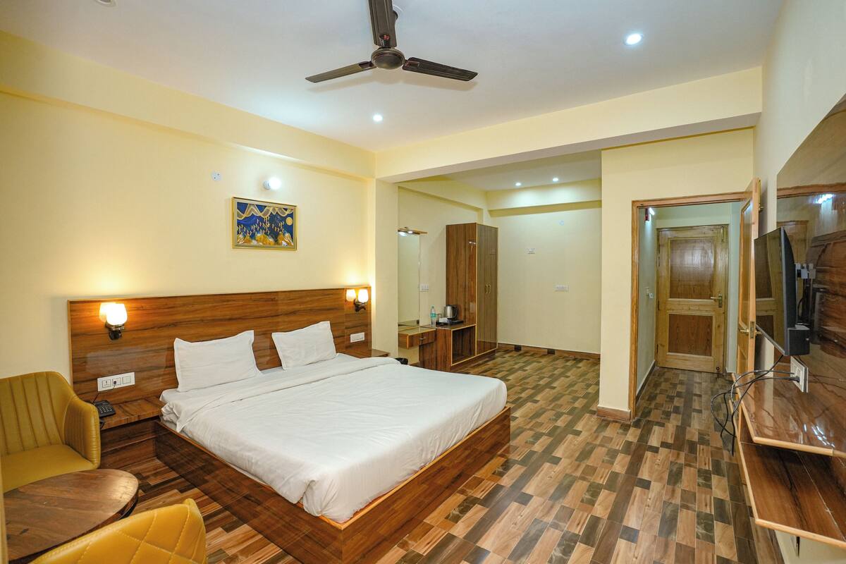 A hotel room with a wooden bed, a desk, a chair, a ceiling fan, and a mirror.