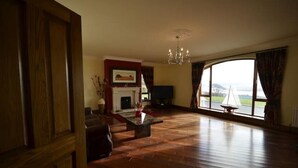 A spacious living room with a fireplace, a television, and a large window with a view of a sailboat.