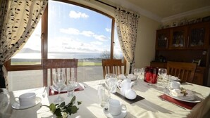 A dining table set with white tableware and a view of the sea.