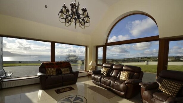 A spacious living room with leather sofas and a large window offering a view of a lake and distant landscape.
