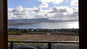 A view from a window overlooking a body of water, fields, and distant hills.