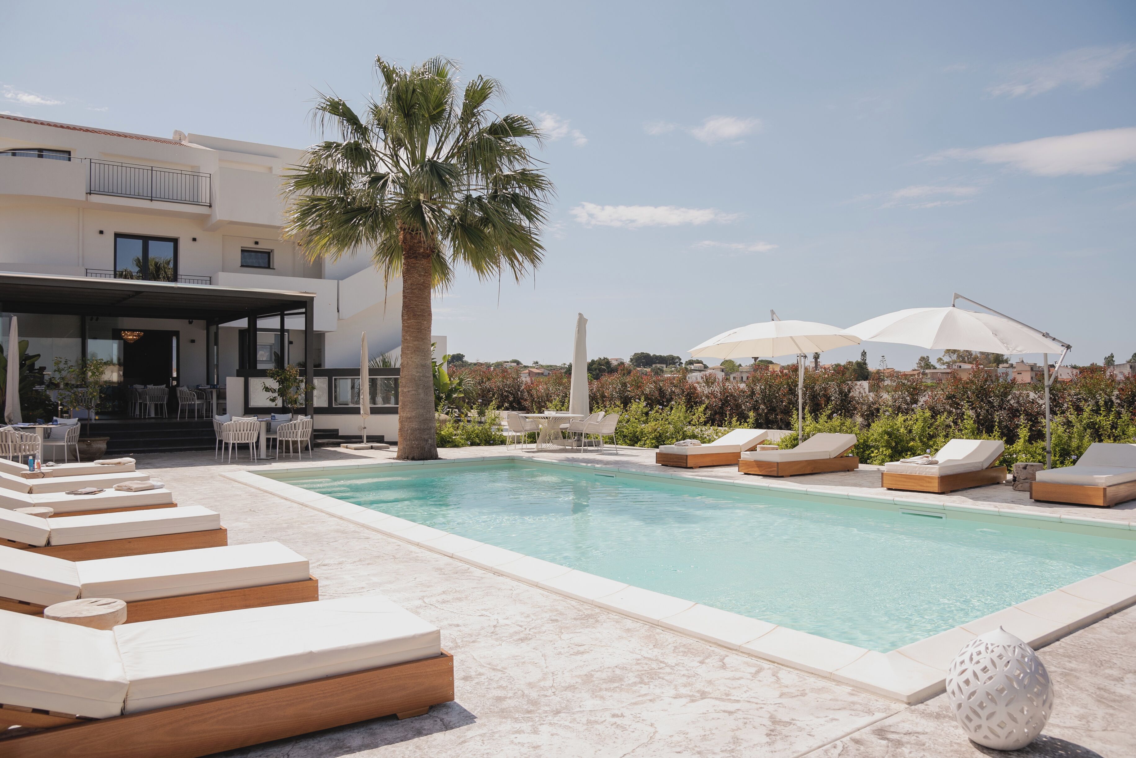 Un espace piscine aménagé avec des chaises longues, des parasols et un palmier.