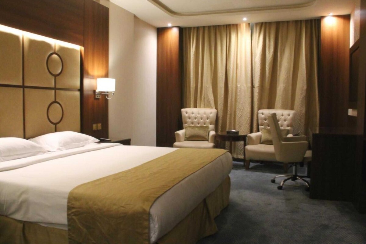 A hotel room with a large bed, two armchairs, a small table, and a desk.