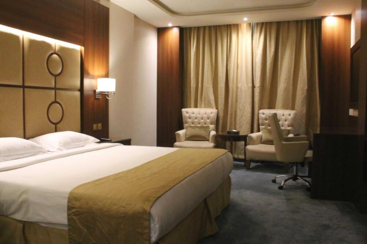 A hotel room with a large bed, two armchairs, a small table, and a TV.