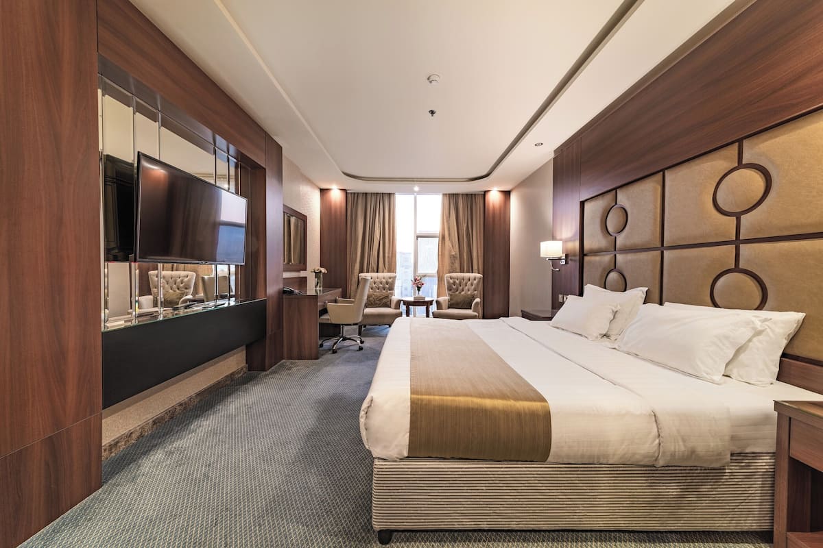 A hotel room with a large bed, a flat-screen TV, a desk with a chair, and a large mirror.