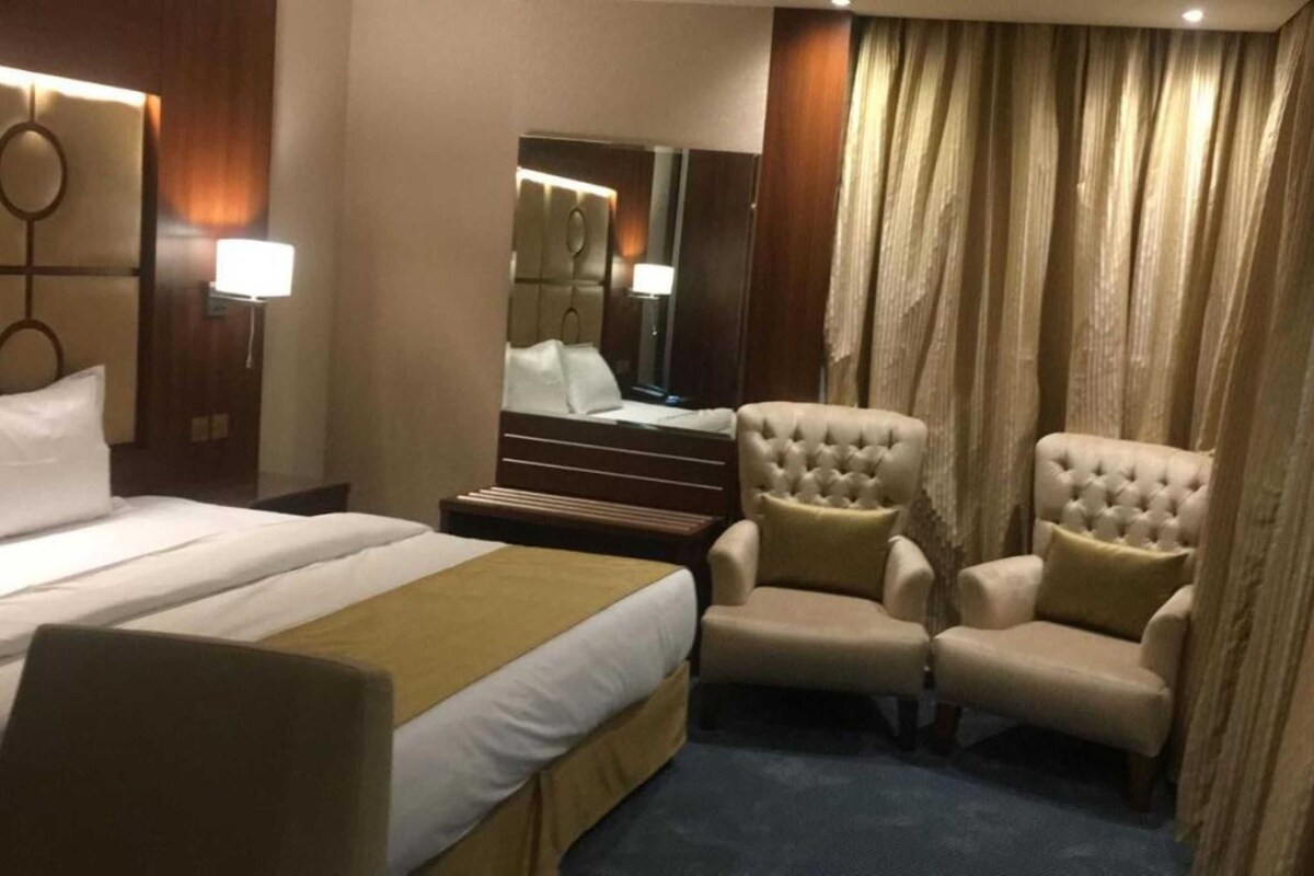 Habitación de hotel con una cama grande, dos sillones, un espejo y vista al interior de la habitación.