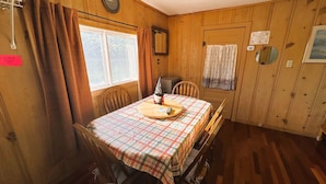 Un coin repas avec une table et des chaises en bois, une horloge au mur et une fenêtre avec des rideaux.