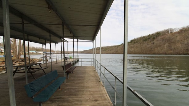 Une terrasse en bois couverte, dotée de bancs et de tables de pique-nique, qui offre une vue sur une rivière paisible.