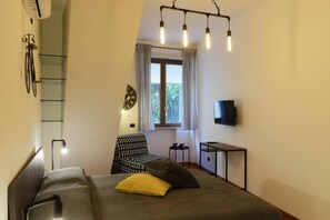 A bedroom with a bed, a chair, a TV, a window with curtains, and a bike rack. - Napoli Vesuvio Industry By Dimorra (NAPOLI)