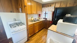 A compact kitchen with wooden cabinets, a stove, a sink, and a refrigerator.
