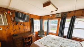 A bedroom with a bed, a desk, a chair, a television, and windows with curtains.