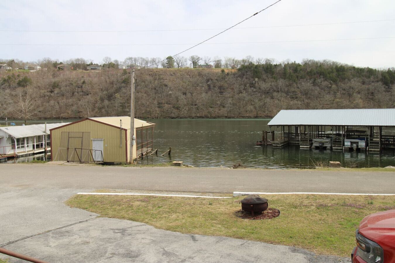 A lakeside property with a small dock, a covered boat house, and a building with a garage.