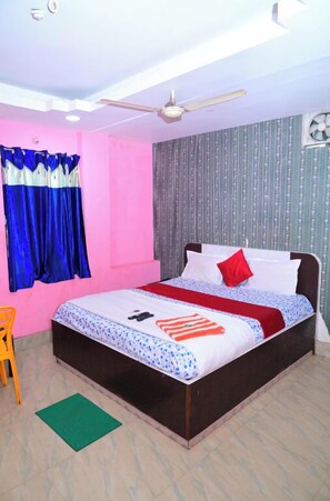 A bedroom with a bed, a ceiling fan, a window with curtains, and a green mat on the floor. - DhamStay Hotel Padoshi Near Beach Puri (Brahmagiri)