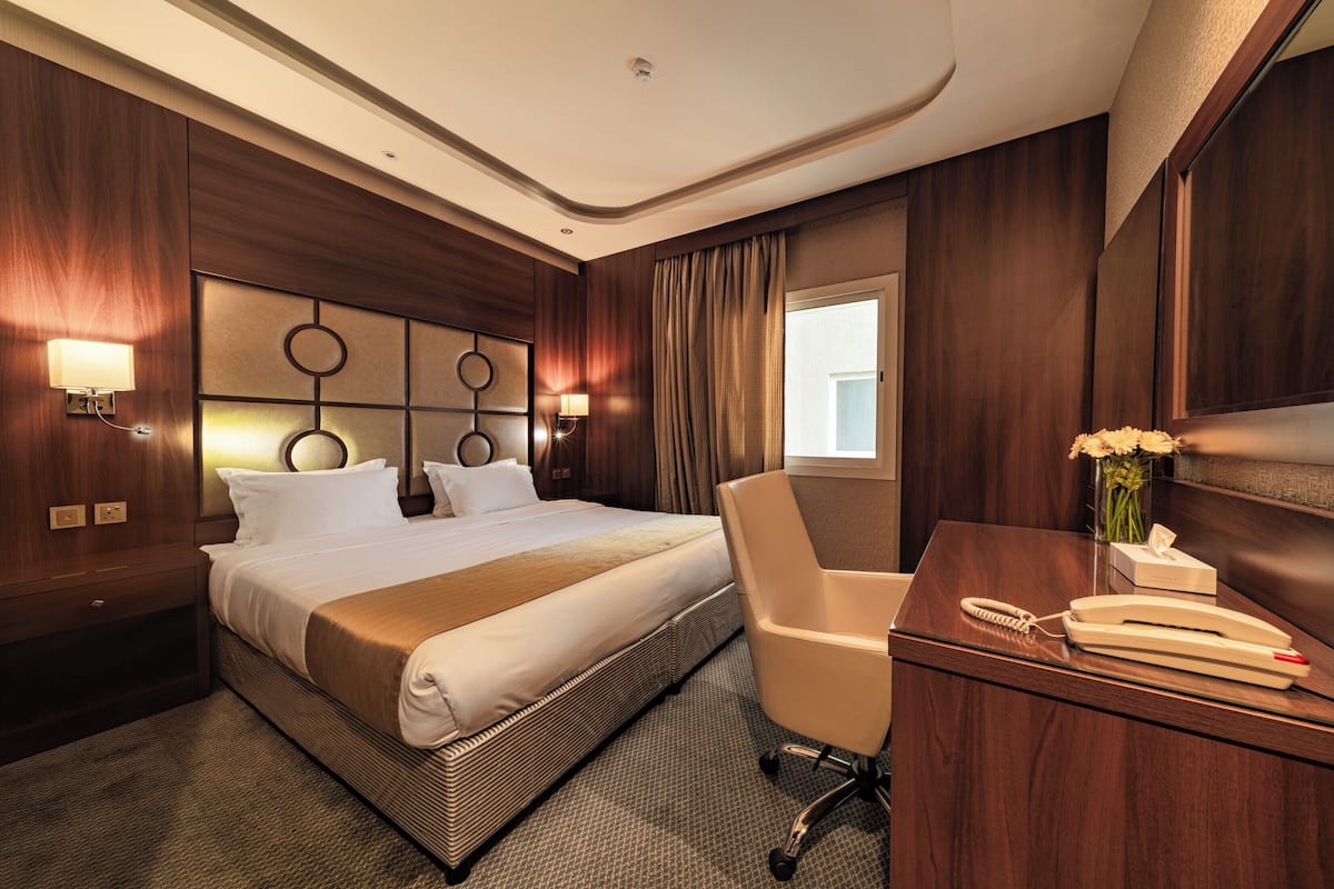 Ein Hotelzimmer mit einem großen Bett, einem Schreibtisch mit Telefon und einer Blumenvase.