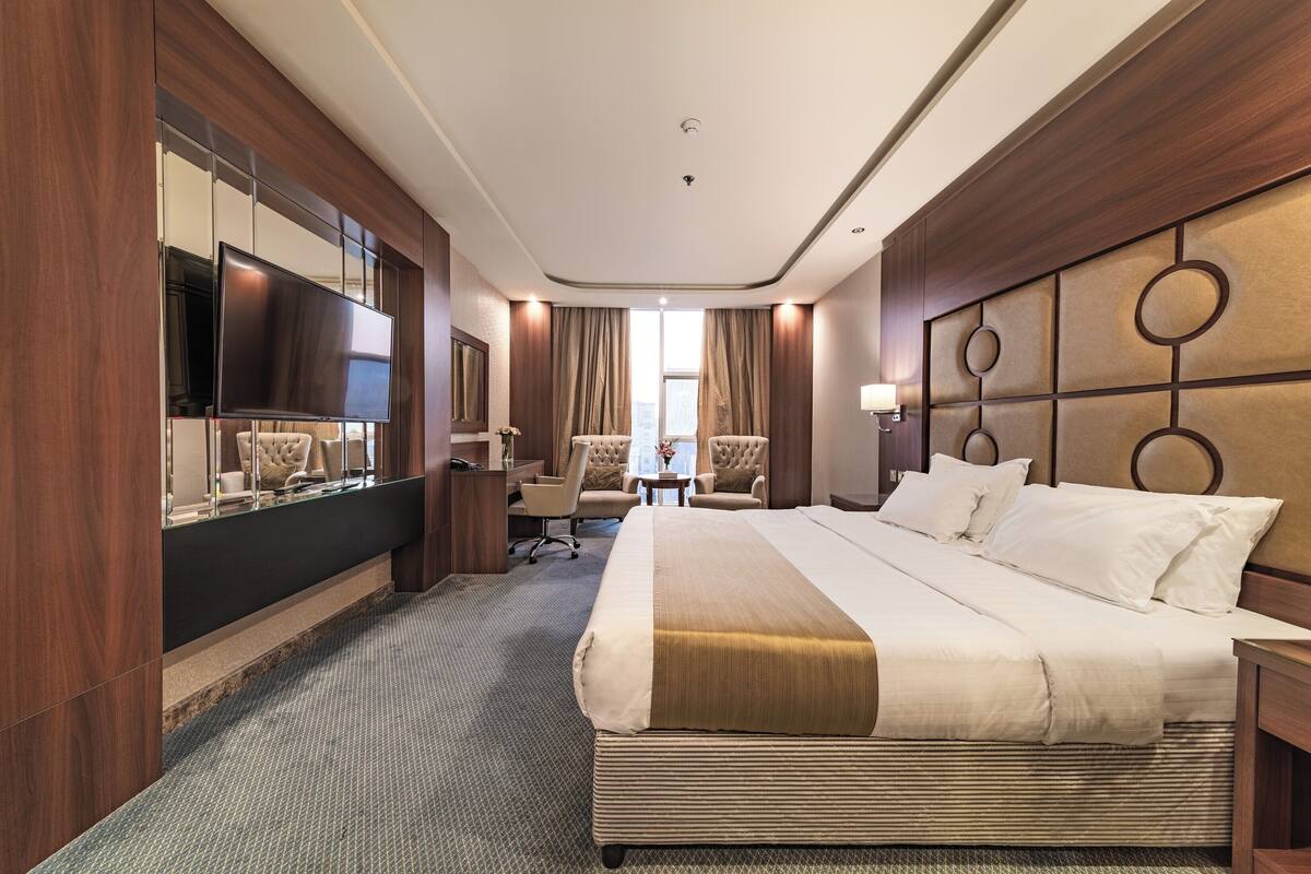 Ein Hotelzimmer mit einem großen Bett, einem Flachbildfernseher, einem Schreibtisch mit Stuhl und einem großen Spiegel.