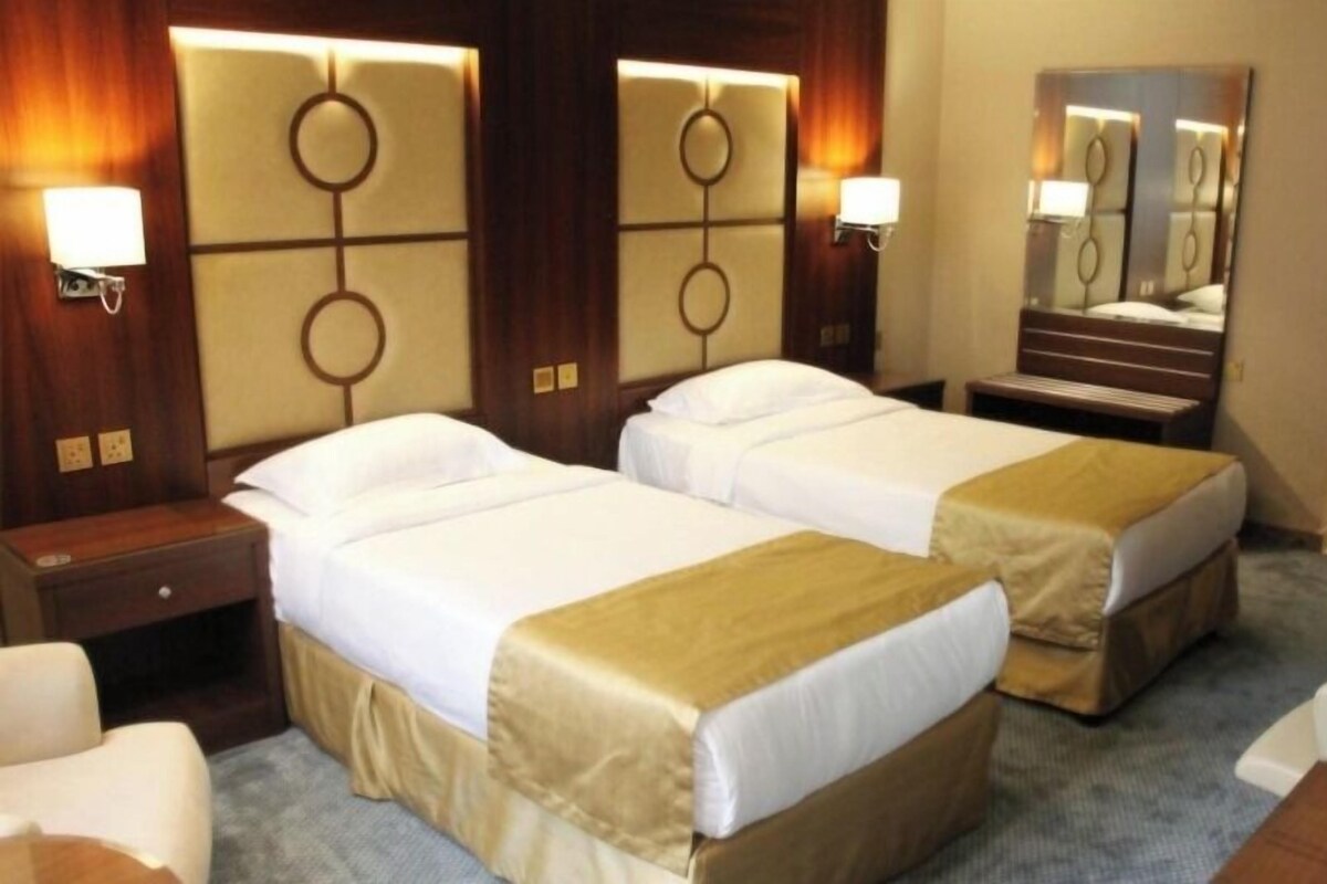 Une chambre d’hôtel avec deux lits, une table de chevet, une chaise, un bureau et un miroir.