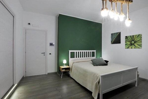 A bedroom with a bed, a nightstand, a lamp, and a green accent wall.