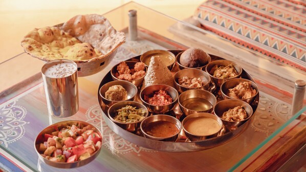 A traditional Indian meal with various dishes in metal bowls, a samosa, and a cup of tea on a patterned tablecloth. - NIrali Dhani Ethnic Resort (Jodhpur)
