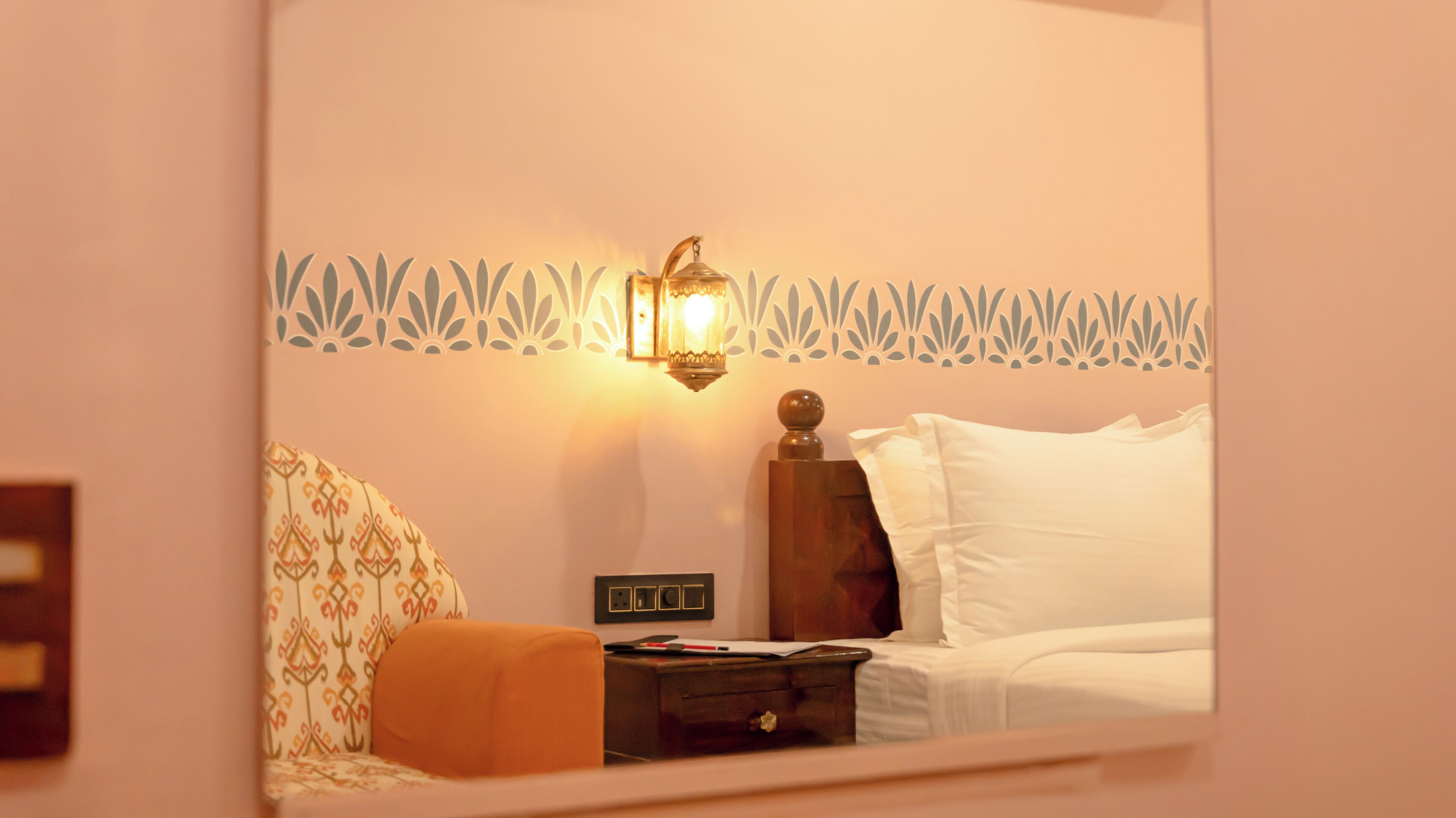 A hotel room with a bed, a nightstand, a lamp, and a decorative wall pattern.