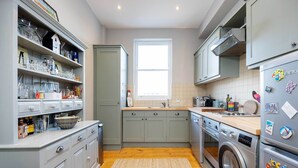 Une cuisine compacte avec des meubles gris, un lave-linge et une fenêtre qui laisse entrer la lumière naturelle.