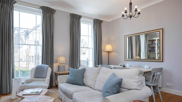 Un salon comprenant un canapé, des fauteuils, une table basse, une lampe, un miroir et une bibliothèque.