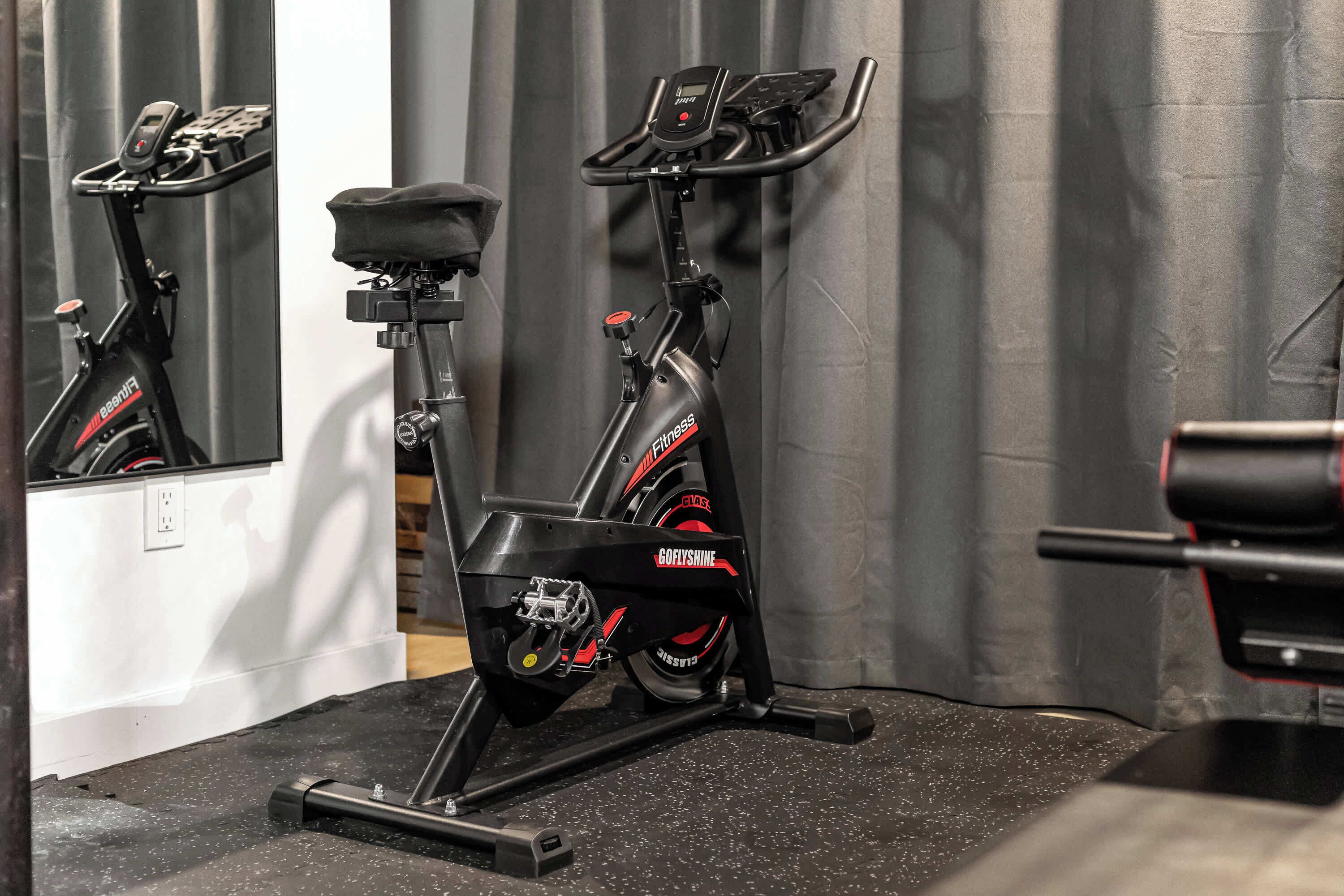 An exercise bike with a digital display and a control panel, positioned in a room with a mirror and a curtain.