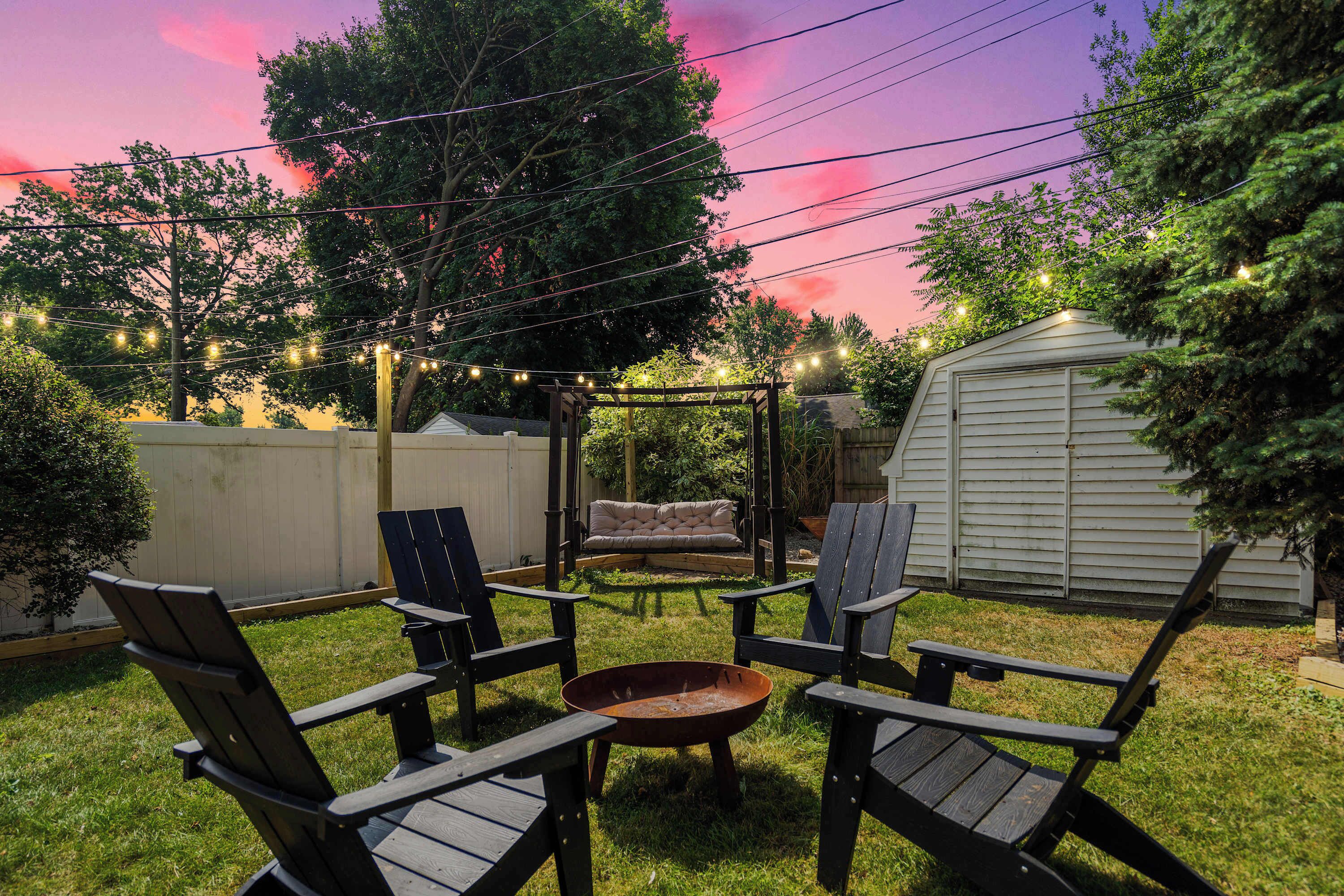 A backyard with a fire pit, outdoor seating, and string lights.