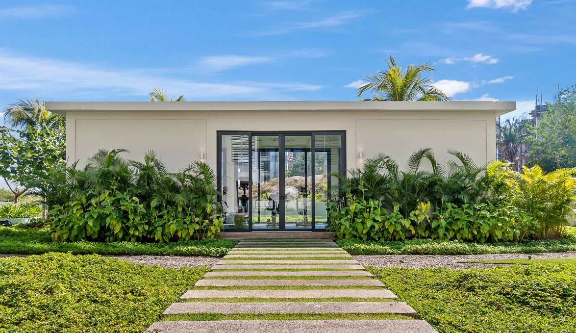A modern building with a glass entrance, surrounded by lush greenery.