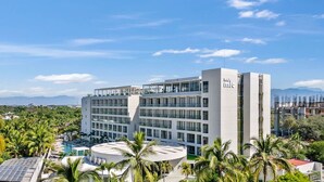 A modern hotel with multiple floors, a rooftop pool, and surrounding greenery.