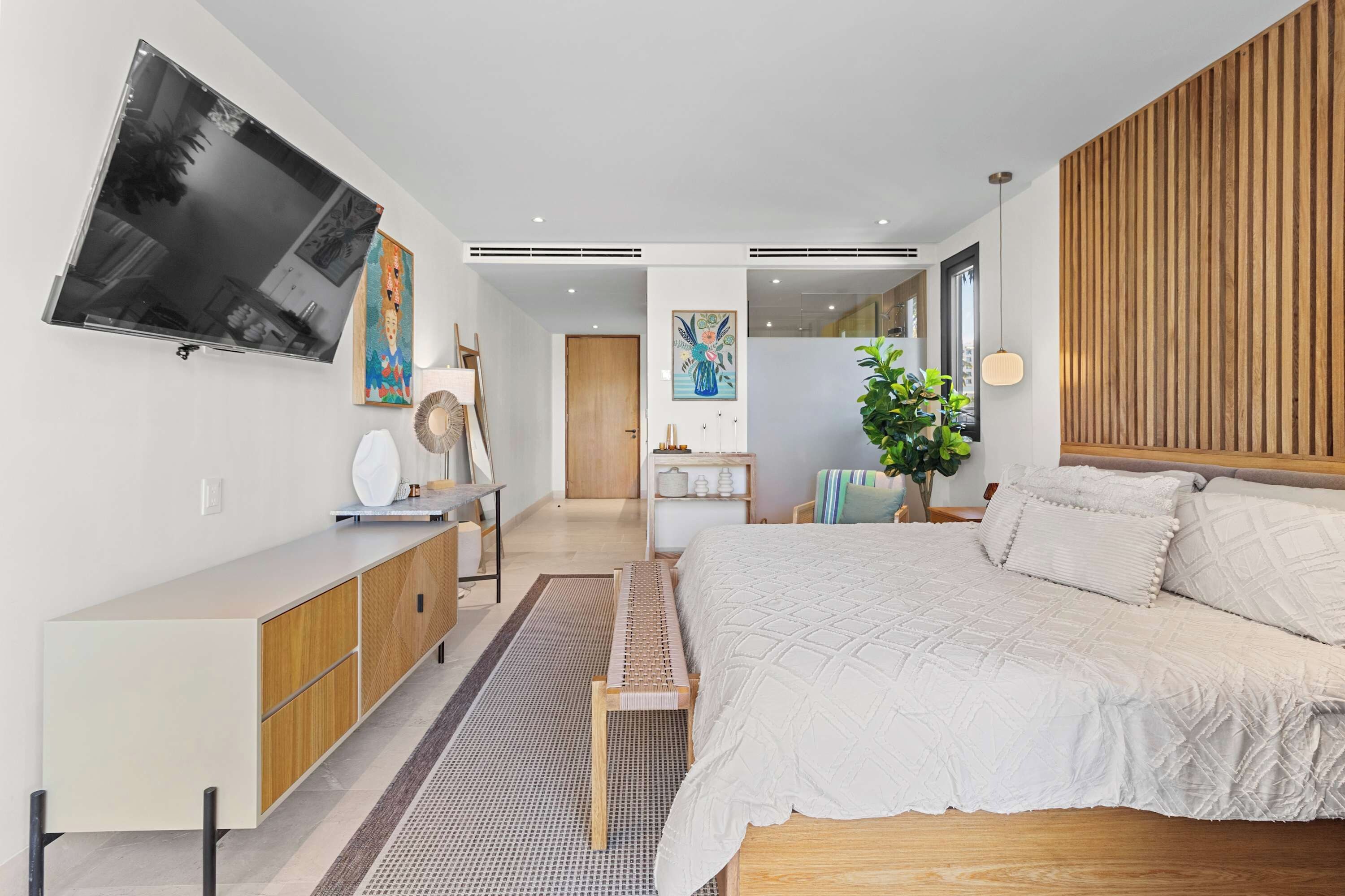 Een moderne slaapkamer met een groot bed, een tv aan de muur, een houten hoofdbord en een nachtkastje.