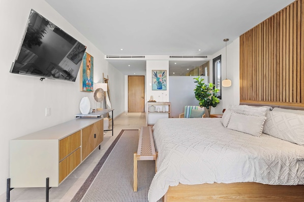 Un dormitorio moderno con una cama grande, un televisor montado en la pared, un cabecero de madera y una mesita de noche.