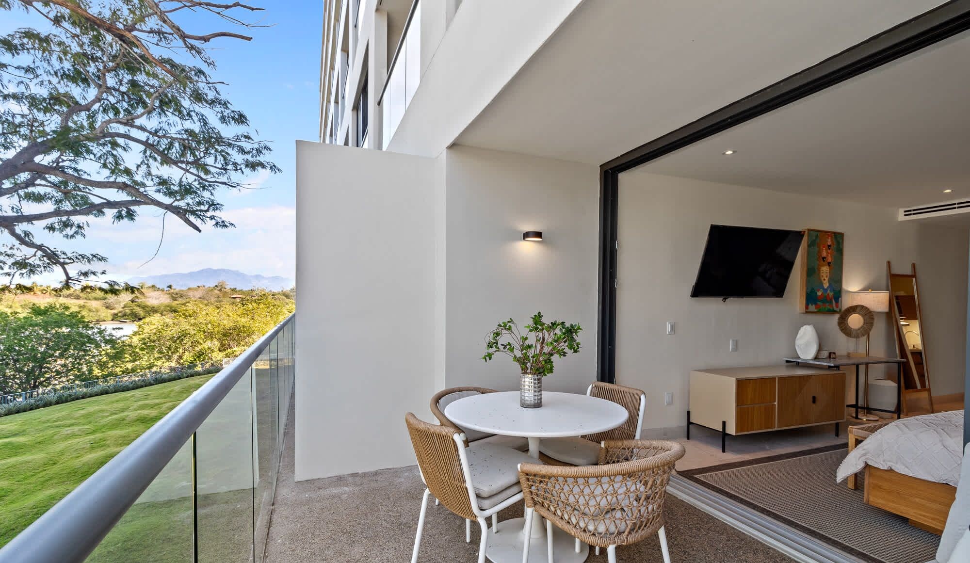 Ein Balkon mit Esstisch und Stühlen, einer kleinen Pflanze und Blick auf eine natürliche Landschaft.
