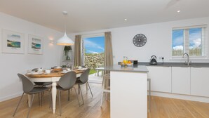 A modern kitchen with a central island, a dining area with a wooden table and chairs, and a view of the outdoors through a glass door.