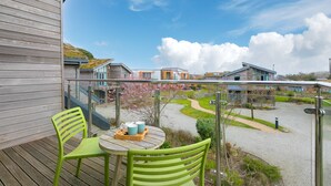 A balcony with two green chairs and a table, overlooking a residential area with houses and a garden path.