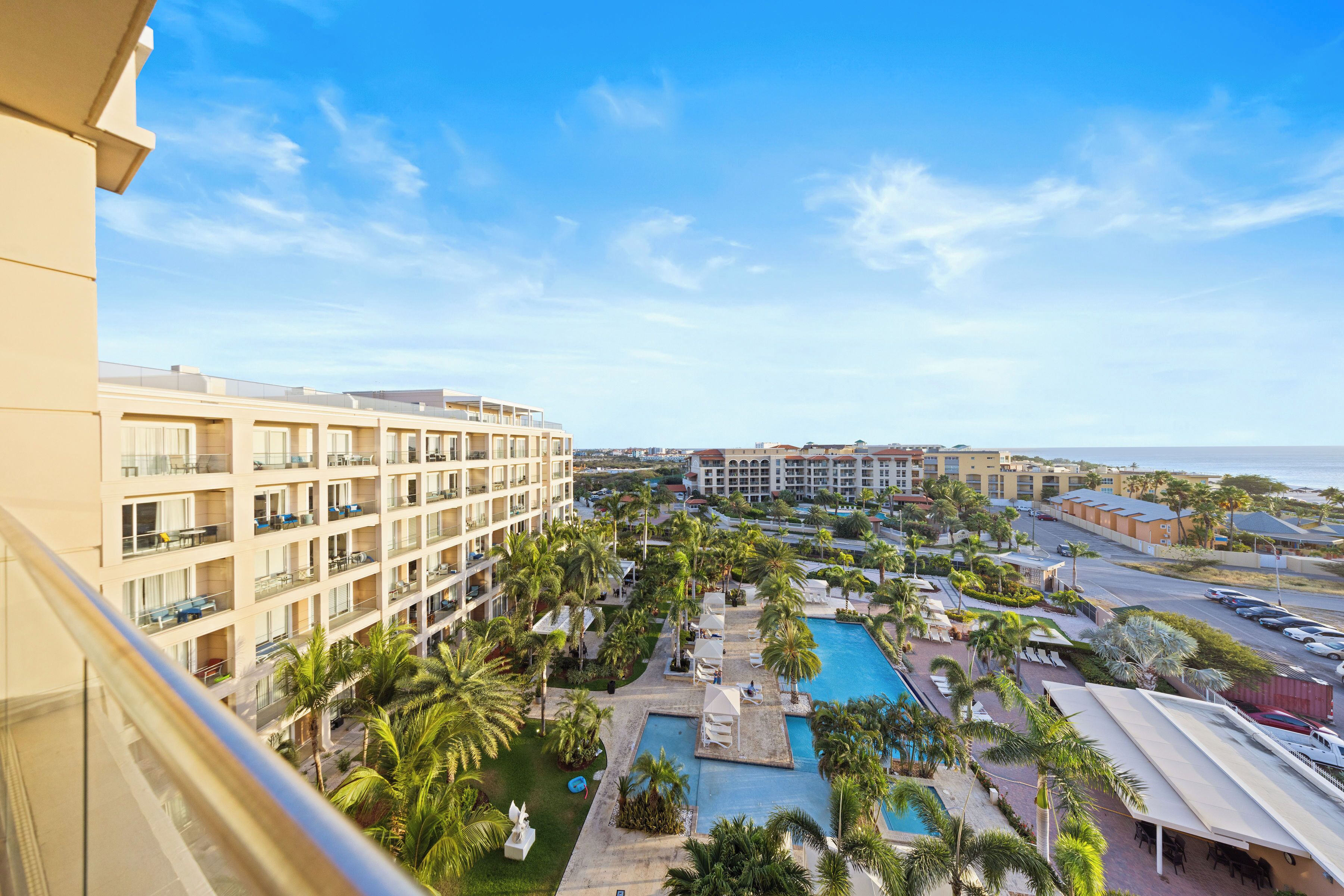 A hotel with multiple balconies, a swimming pool, and a view of the ocean.