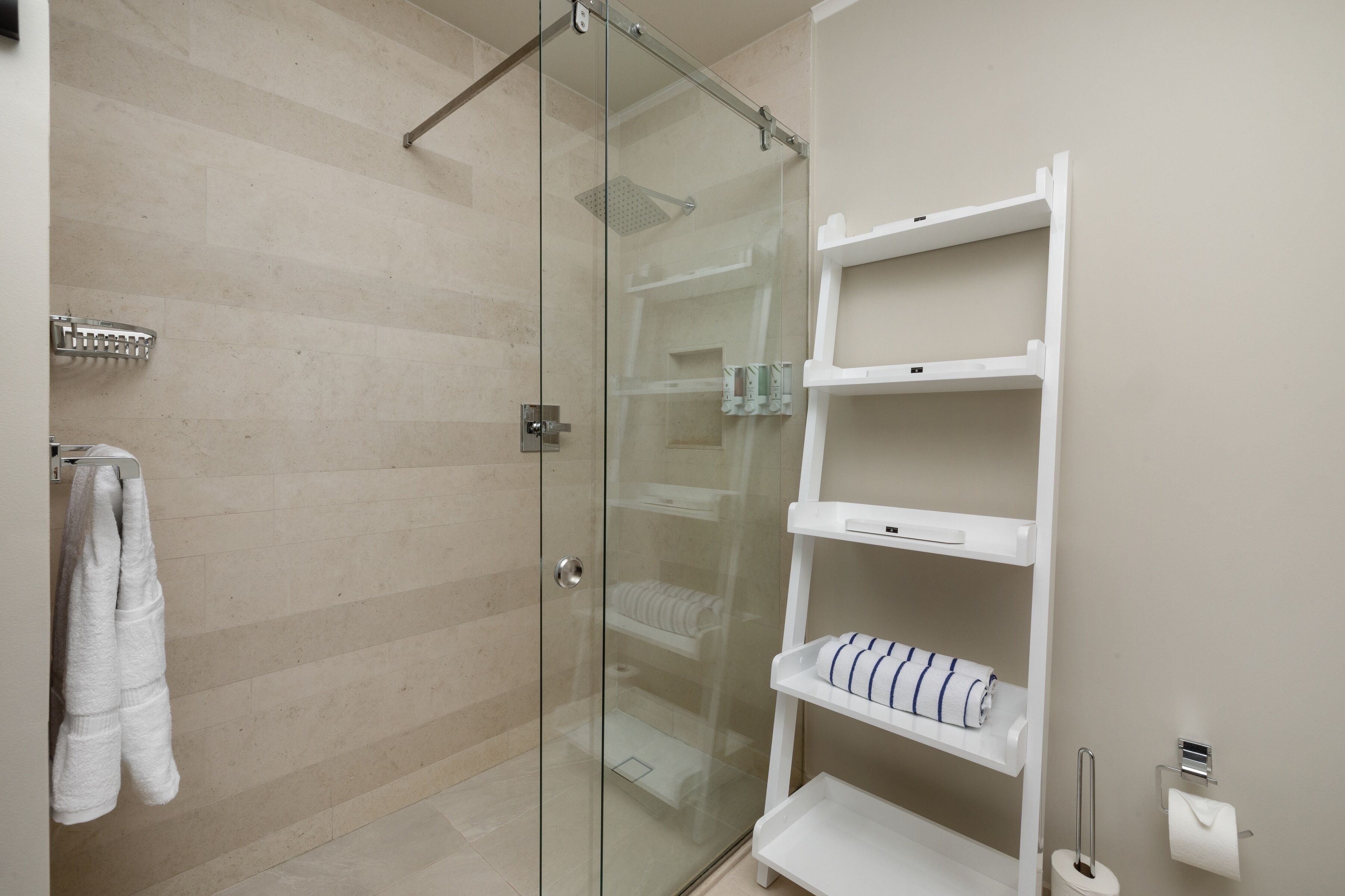 A modern bathroom with a glass-enclosed shower, white shelves with towels, and a toilet paper holder.