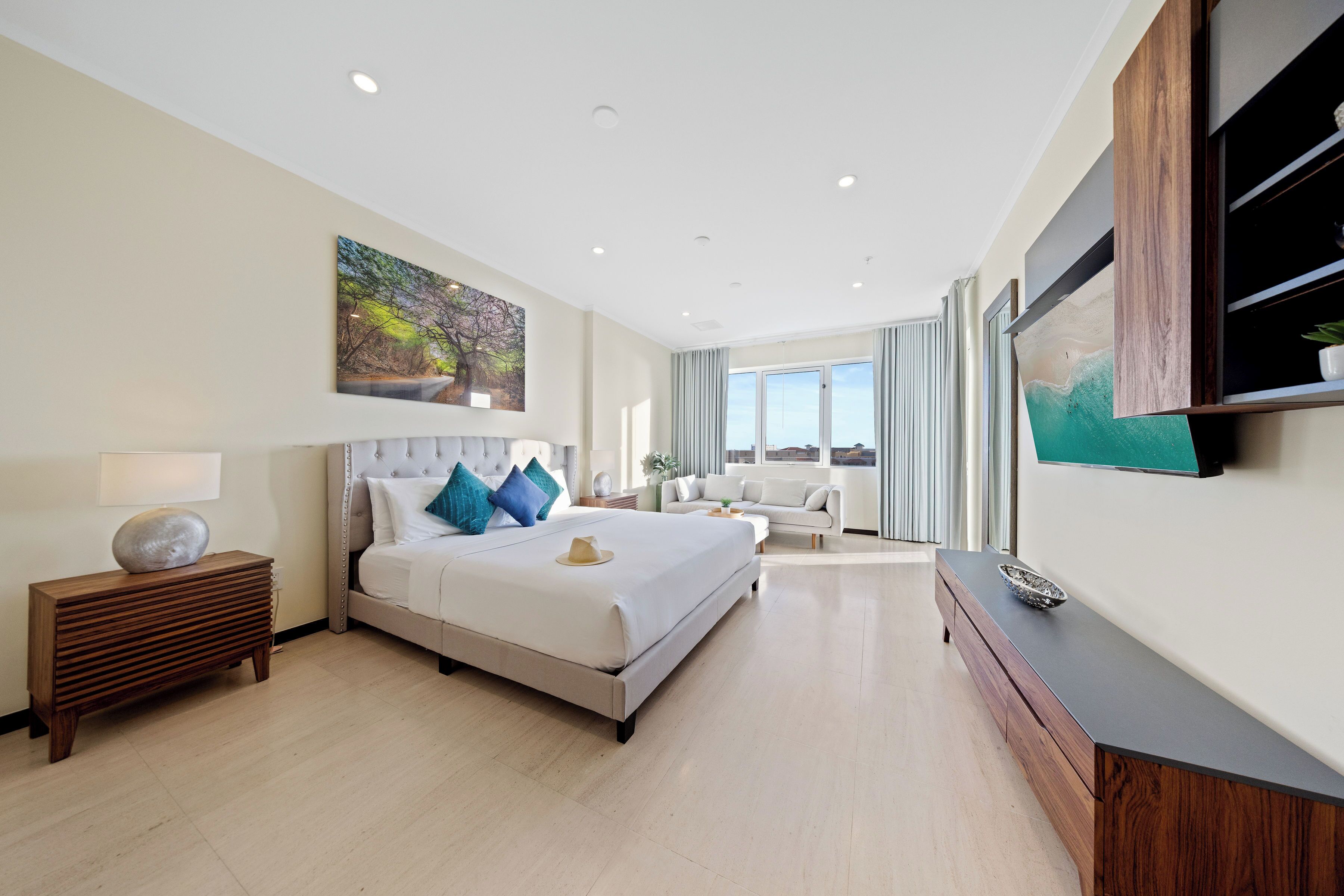 A modern hotel room with a large bed, a wooden nightstand, a flat-screen TV, and a view of the outdoors.