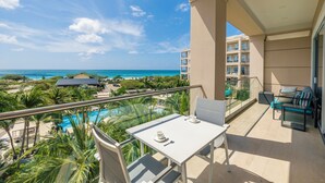A balcony with a table and chairs, overlooking a pool and beach area. - Bocobay LeVent Condos (Oranjestad)