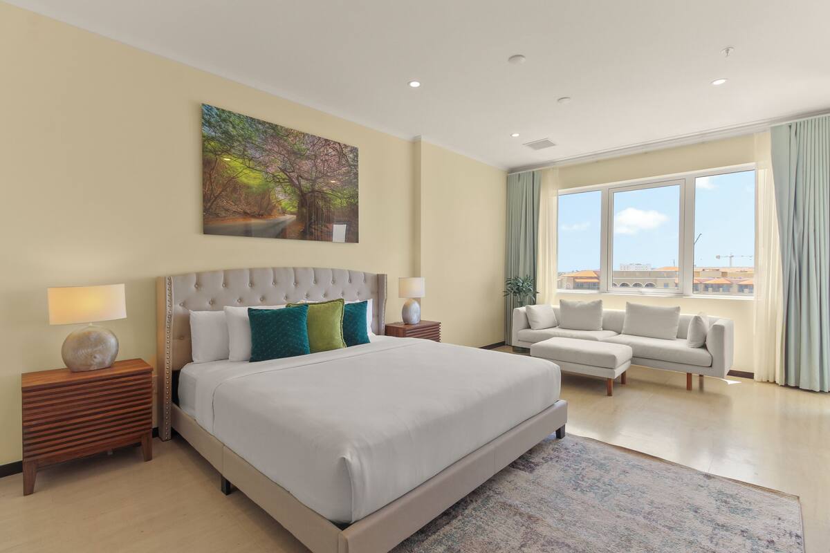A spacious bedroom with a large bed, a sofa, and a view of the city.