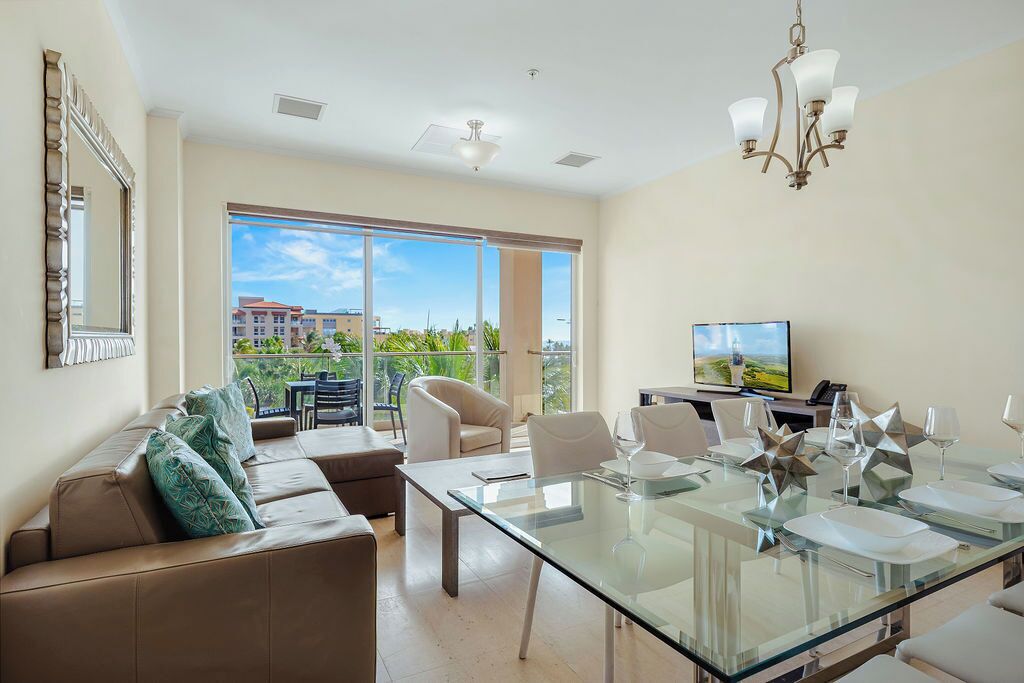A modern living room with a glass dining table, leather sofa, and a TV on a stand.